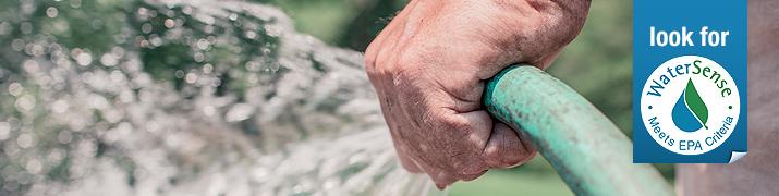 Persona regando el césped con una manguera.