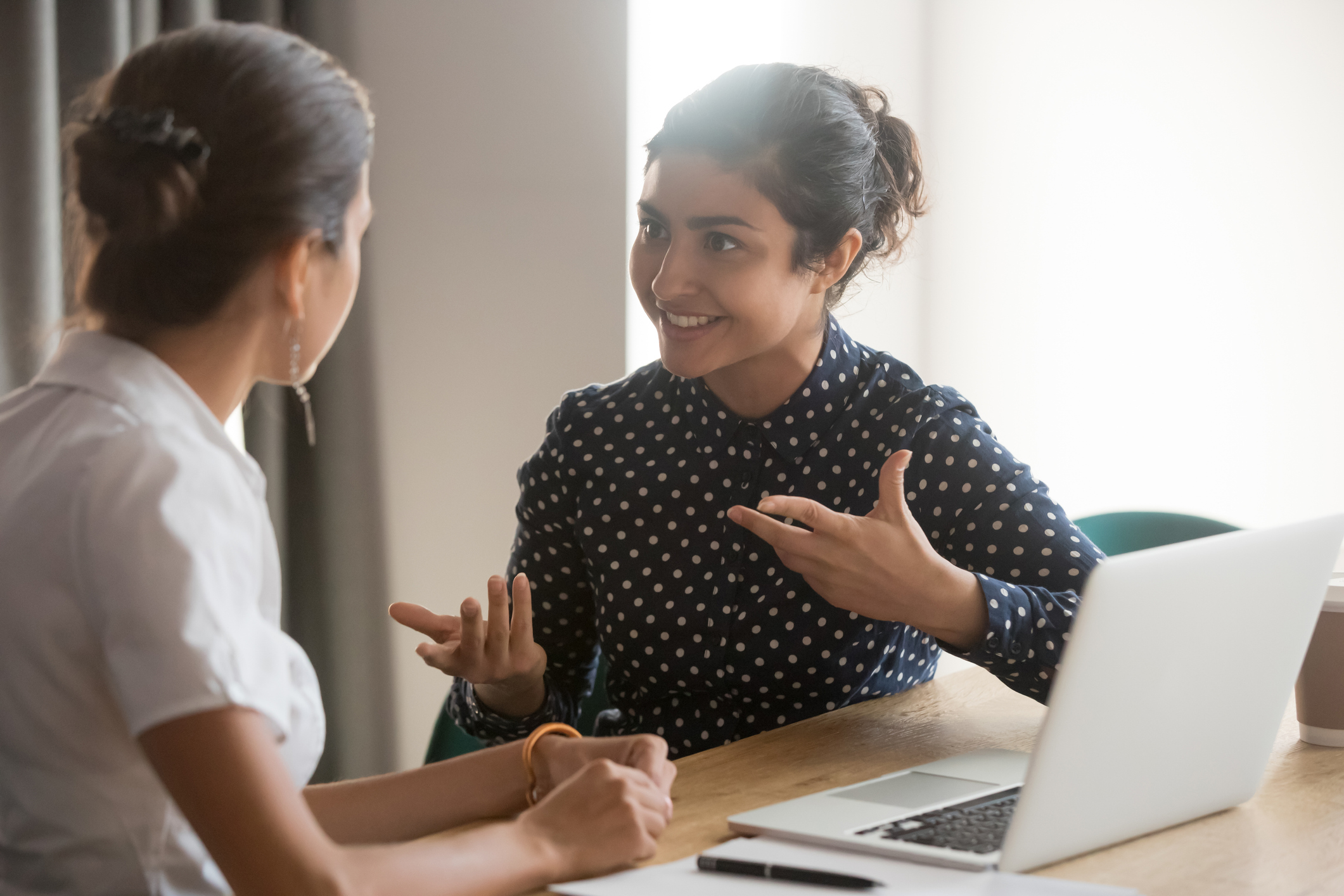 Dos mujeres hablando con una computadora laptop frente de ellas